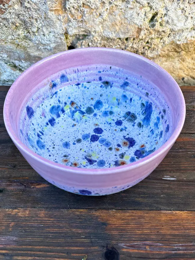 Shoreline Small Bowl, a colourful bowl placed on a wooden surface in front of a brick wall. 
