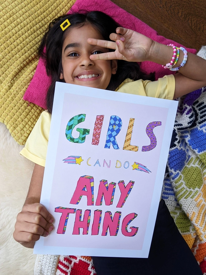 Young girl lying down holding an art print saying 'Girls can do anything'