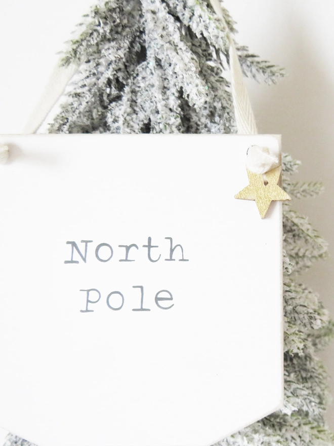 painted white banner with North Pole message strung with cotton and decorated with a wooden gold star.