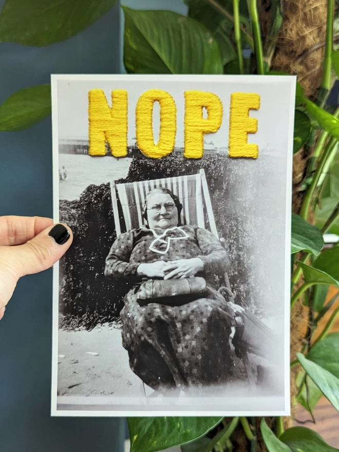  B & W photo print of woman with yellow embroidered ‘nope’ held against blue background