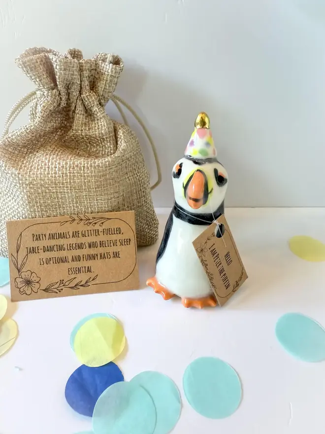 Handmade Porcelain Puffin Penguin Topper With Golden Hat, on a table near party decorations. 