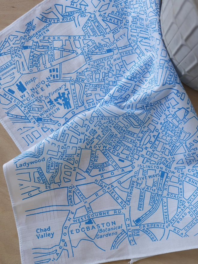 A lifestyle photo of a Mr.PS Birmingham Map hankie printed in sky blue with a concrete plant pot on a plywood table.