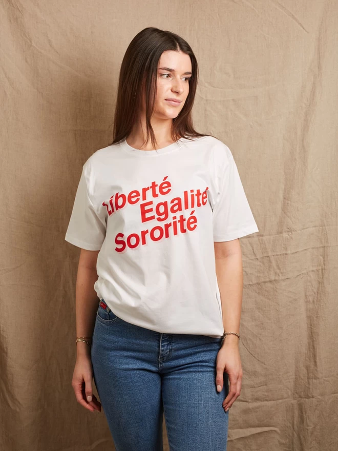 Model wearing a white organic cotton t-shirt with the words  LIBERTÉ, EGALITÉ, SORORITÉ written in red with a pink boarder