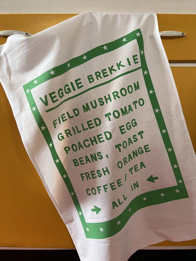 Mr.PS Veggie Brekkie Menu screenprinted Tea Towel hanging on a yellow kitchen cabinet