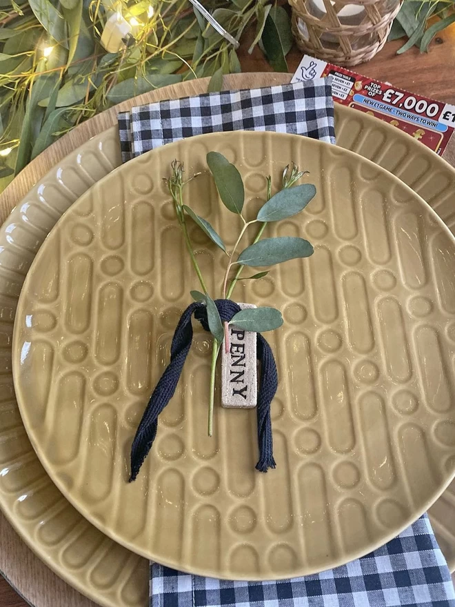 yellow dinner plate with a personalised name tag tied around a sprig of foliage