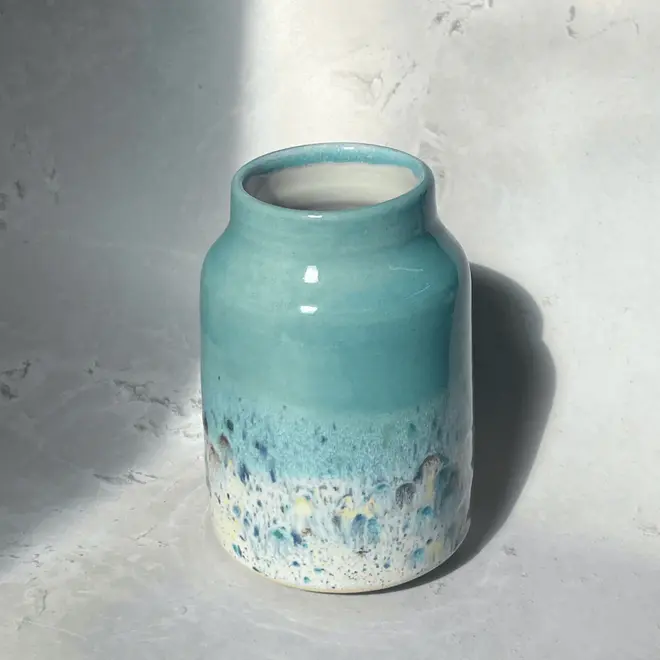 Shoreline Large Vase, a colourful vase placed on a stone surface in front of a plain backdrop. 