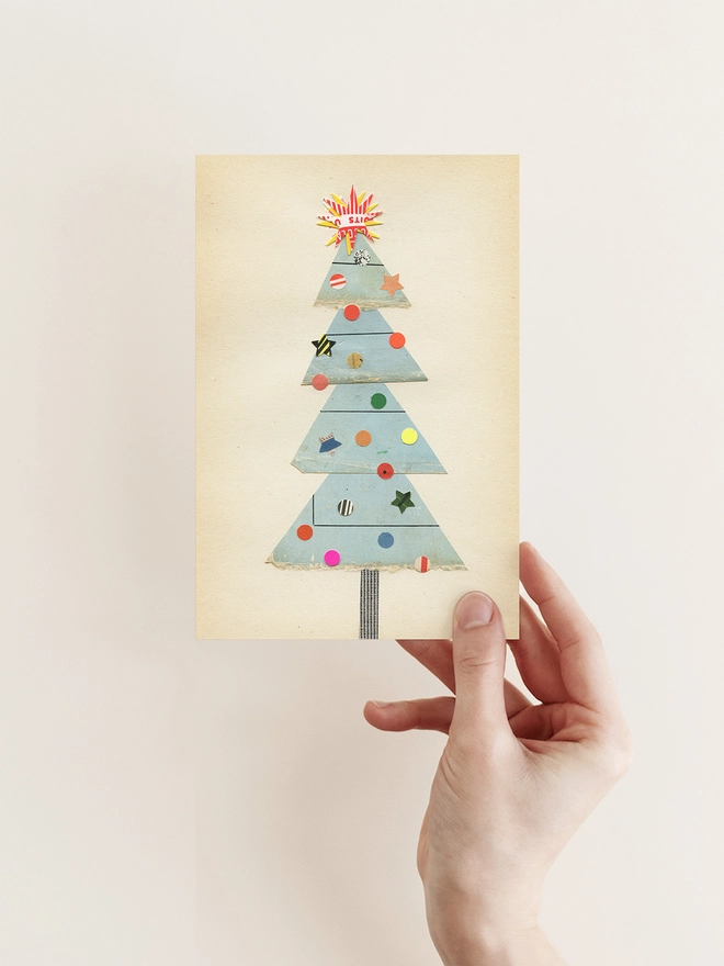 A charming Christmas card featuring a pale blue tree with a collection of eclectic decorations and a large star on top.