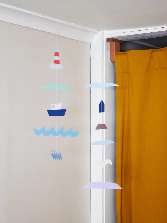 Two paper mobiles hanging in front of a curtain in the corner of a room. One is sea themed and one is land themed. 