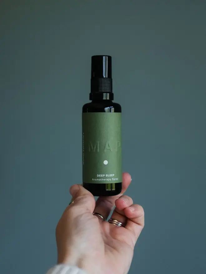 deep sleep lavender and vetiver home fragrance spray. bottle photographed held against forest green backdrop.
