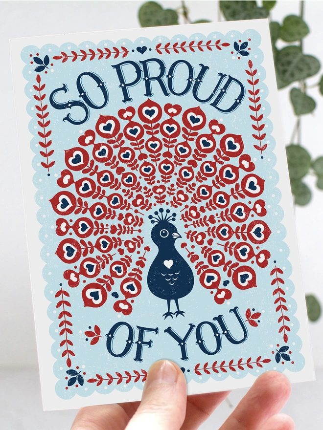 hand holding proud of you peacock card in red white and blue