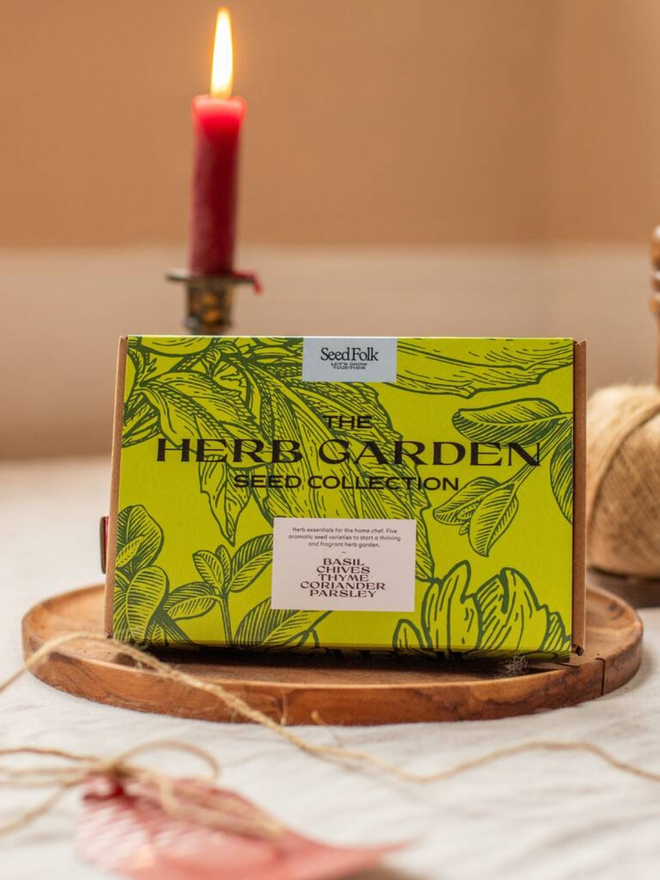 the herb garden seed collection. packaging for seed packets decorated with illustrated green leaf outlines. box photographed in wooden dish on counter.