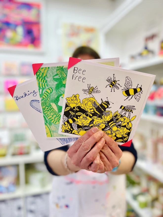 Artist holding riso printed charity card featuring a yellow & black Bee design & the words Bee Free