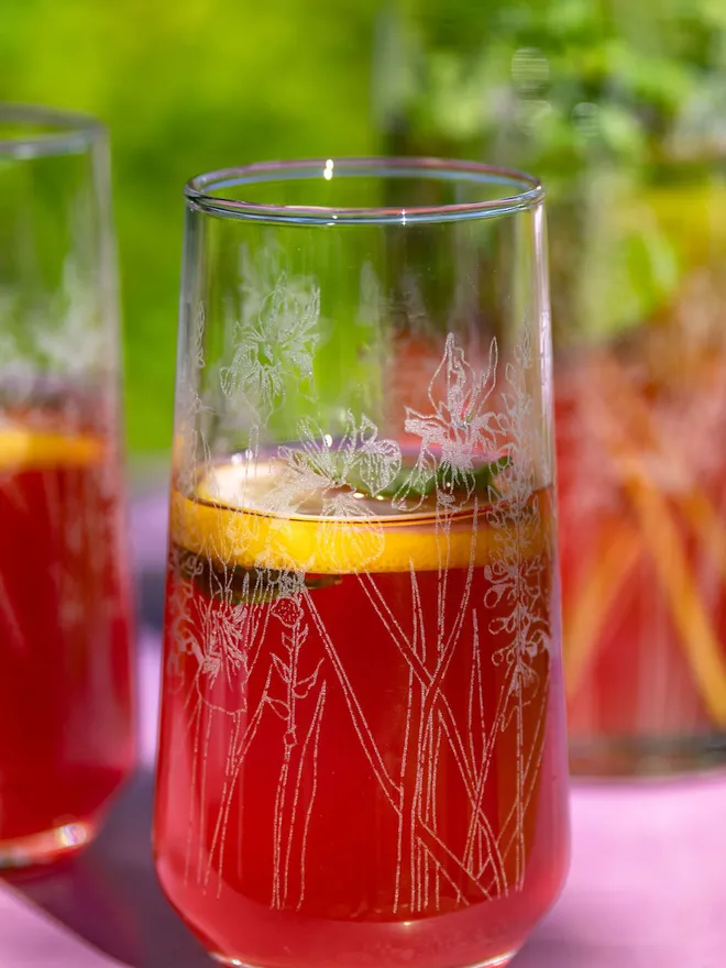 Floral Hiball Glass .A tall, floral-etched highball glasses on an outdoor table.
