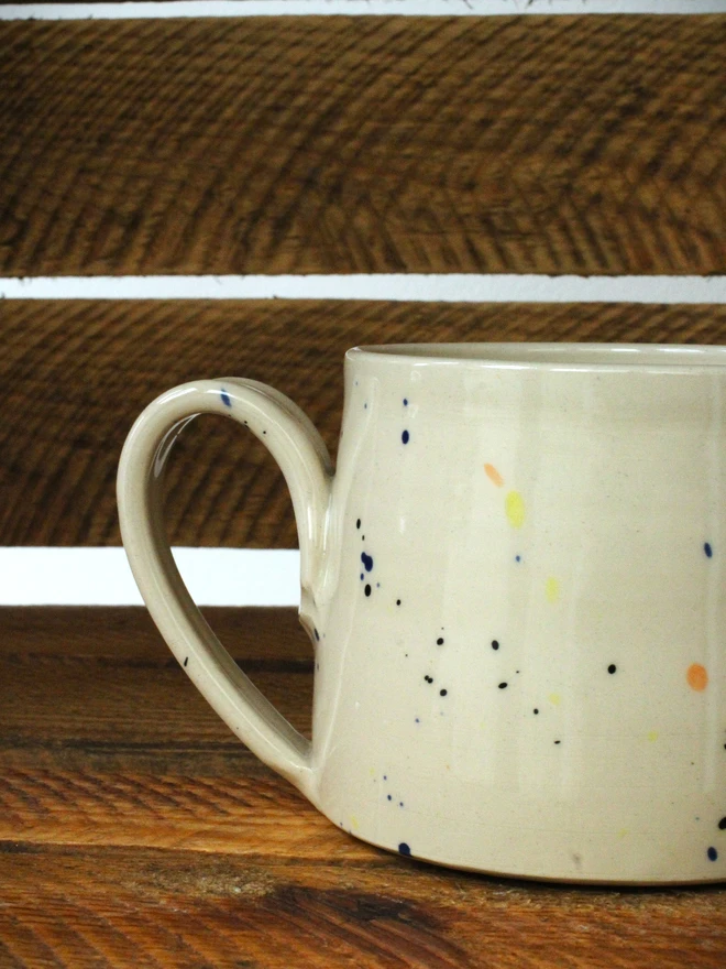 Large creamy white terrazzo cups with black, blue, and yellow splatters and glossy glaze close up on a wooden background