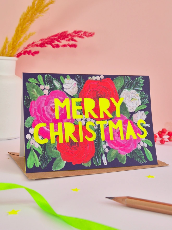 Christmas Card with roses painted on it and a paper cut Merry Christmas Slogan backed with yellow neon paper 