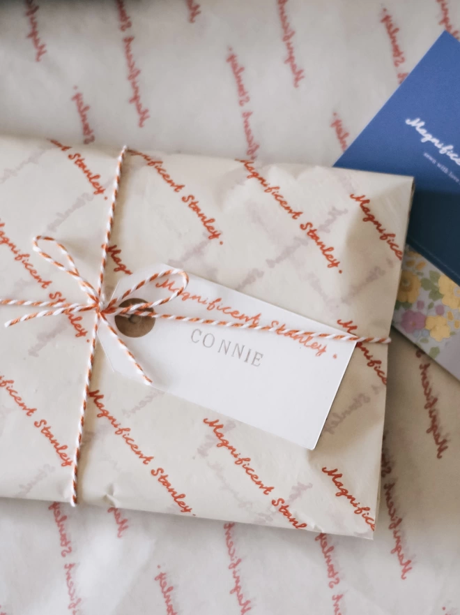 gift wrapped item in logo tissue, tied with orange and white  bakers twine and a hand stamped name tag
