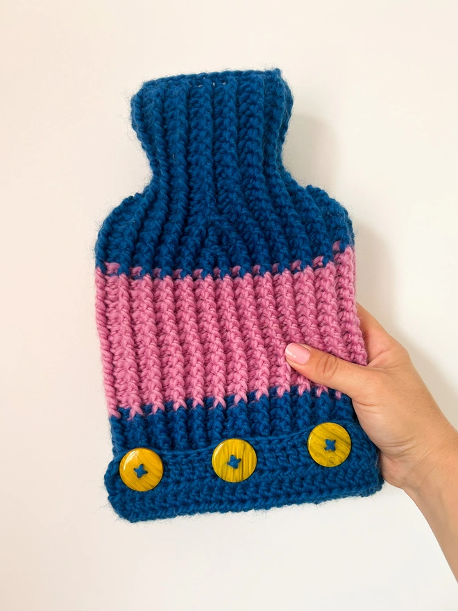 Hand holding hot water bottle handmade in blue and pink 