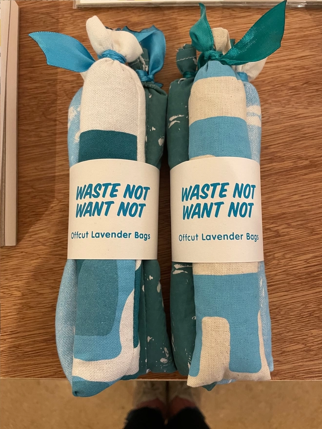Two bundles of lavender bags sit side by side on a wooden counter. They are turquoise theme with bits of screenprinted design on the offcut fabric. Label reads Waste Not Want Not offcut Lavender Bags.