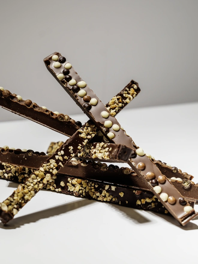 Picture of milk and dark hand cut chocolate strips, topped with cocoa nibs and crispy chocolate spheres, stacked up in a pile 
