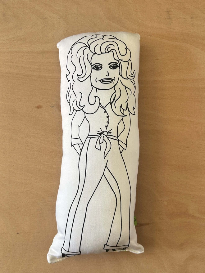 Black and white illustrated screen printed cushion of Dolly Parton. The cushion sits on a light wood surface.