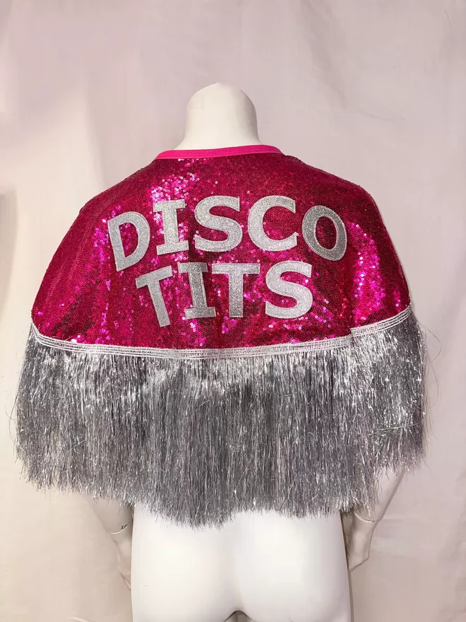 a midi cape with hot pink sequins, silver text reading 'DISCO TITS' and silver tinsel