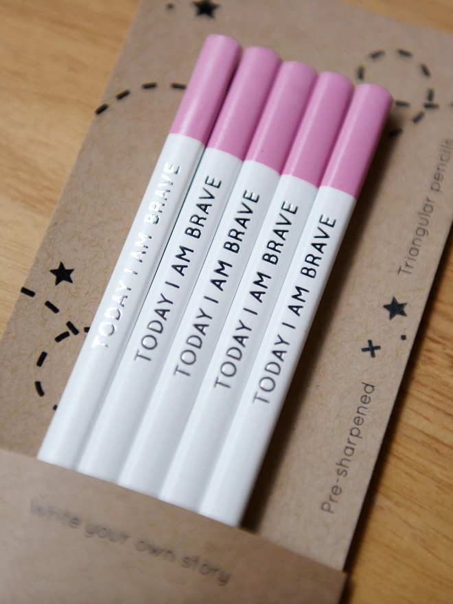 Five white pencils with pink tips and the words Today I Am Brave written along the side, rest on cardboard packaging.