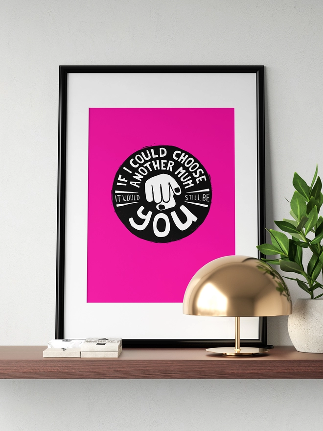 A bright pink framed print sitting on a shelf in a stylish home. The type reads: If I Could Choose Another Mum It Would Still Be You.