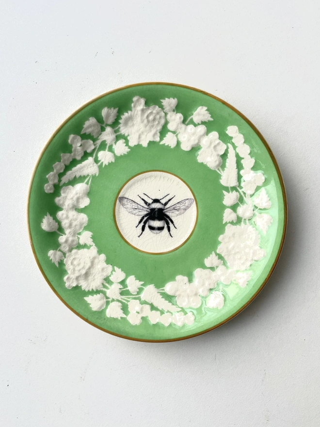 vintage plate is bright green with a white floral border and in the centre is an illustration of a bee