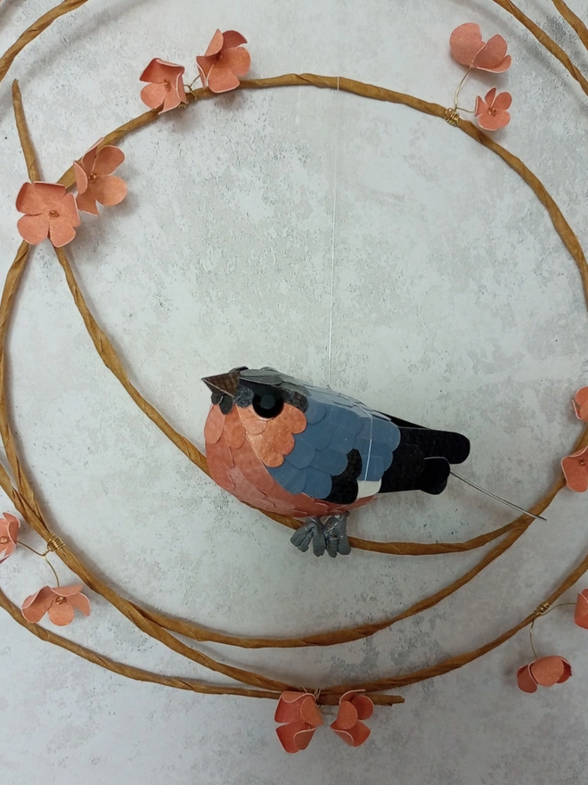 Bullfinch sculpture, perched on a wreath of peach blossom flowers.