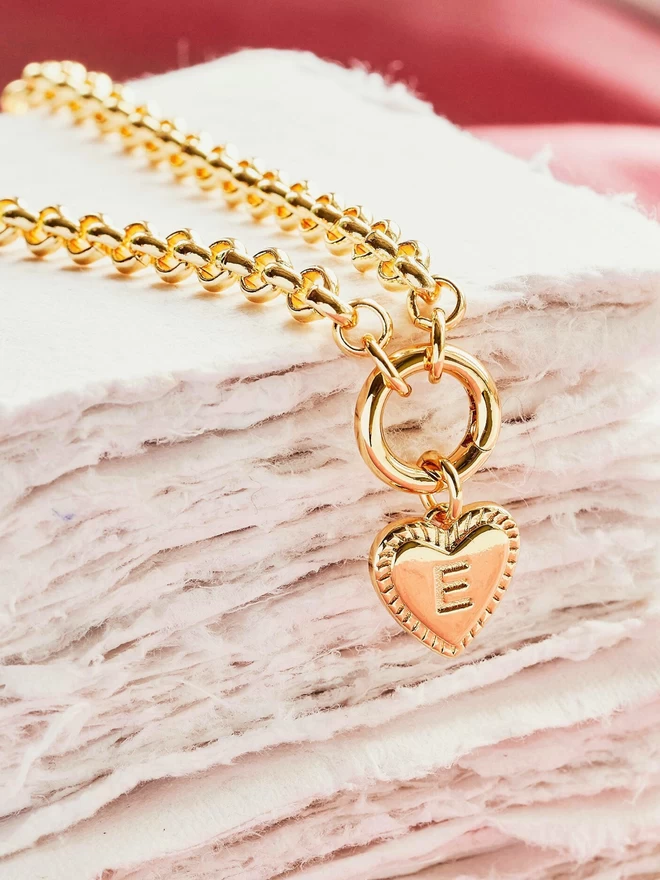 Gold heart charm with the initial E hanging from a gold belcher chain necklace