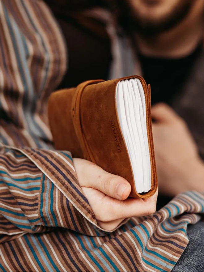 make your own leather journal. a handheld leather journal photographed from the side to show pages inside.