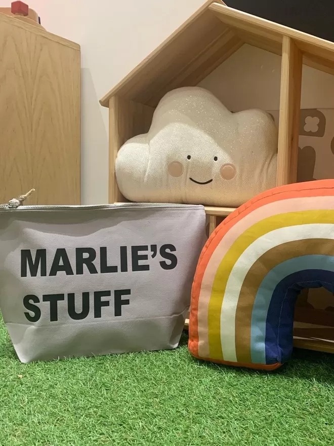 my bags of stuff grey pouch on green fake grass in a playroom with a cloud plushy cushion in the background and a rainbow plushy next to the pouch