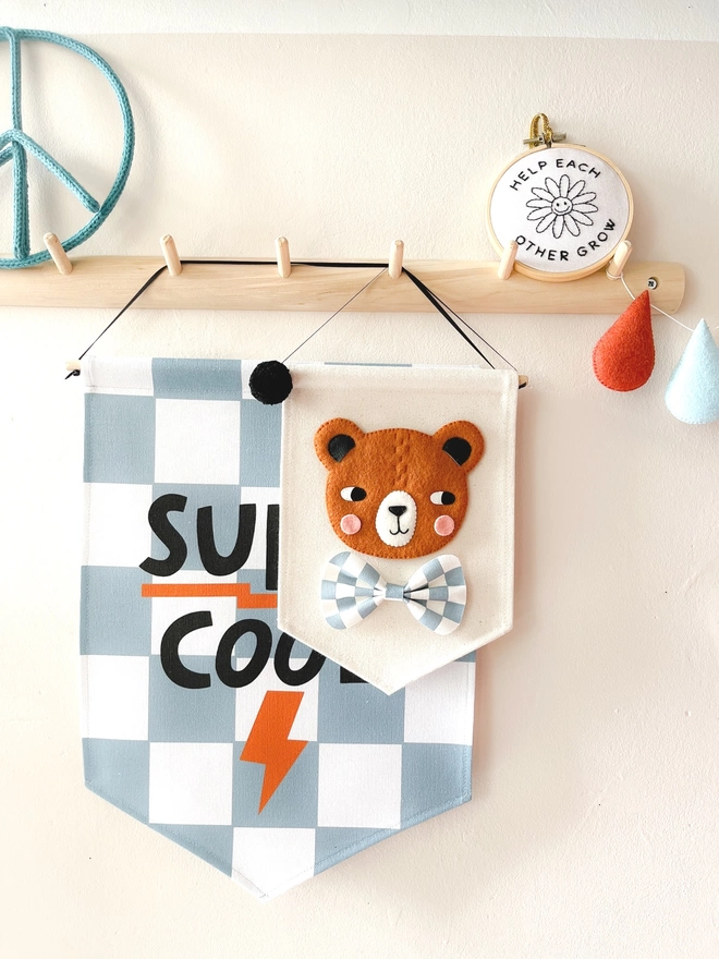 Blue and white chequered super cool banner and a brown bear banner hanging from a wooden peg rail