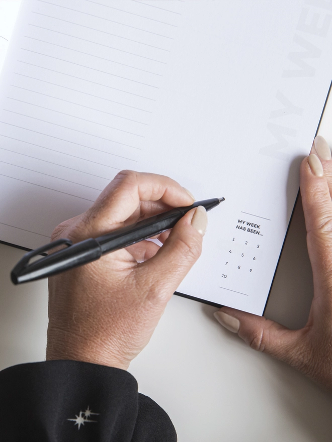 Lady using a black pen to fill in a page of the HELLO TIME planner