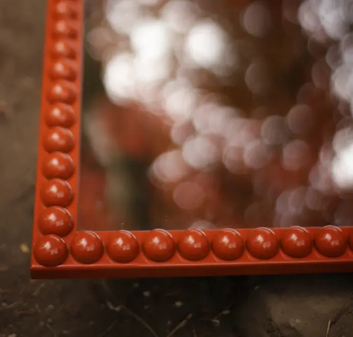 Floor-length bobbin mirror with a turned wooden frame, leaning against a wall on a concrete floor.