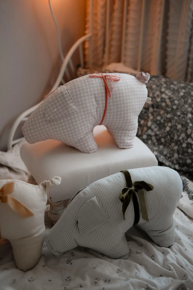 Cotton Pig Pillow Ornament, a pink pillow ornament sitting on a table in a bedroom. 
