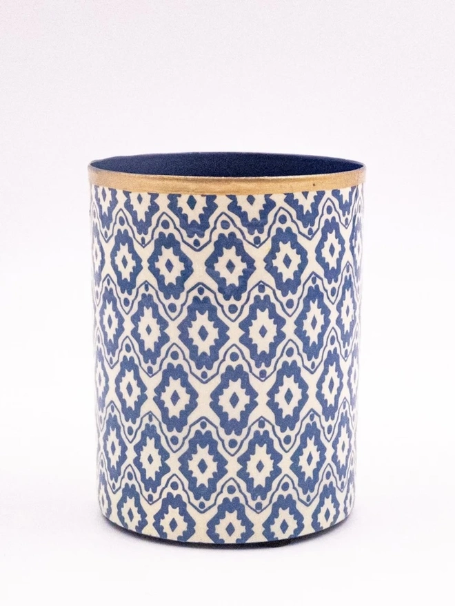 Perfect Enamel Pot. A cylindrical pot covered in blue and cream geometric ikat-style paper, finished with a gold rim and navy interior. This decorative container works as a pen pot, vase holder or bathroom storage.
