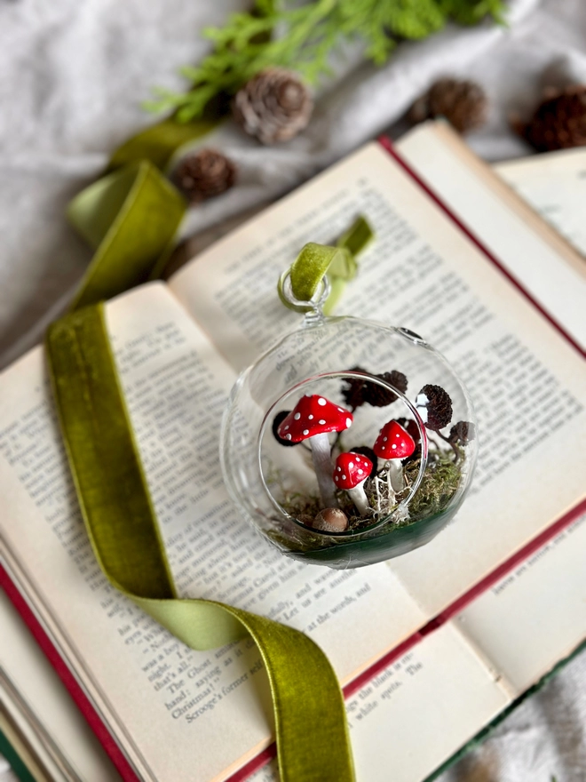Glass Bauble filled with handmade toadstools and alder cones sitting on a vintage book 