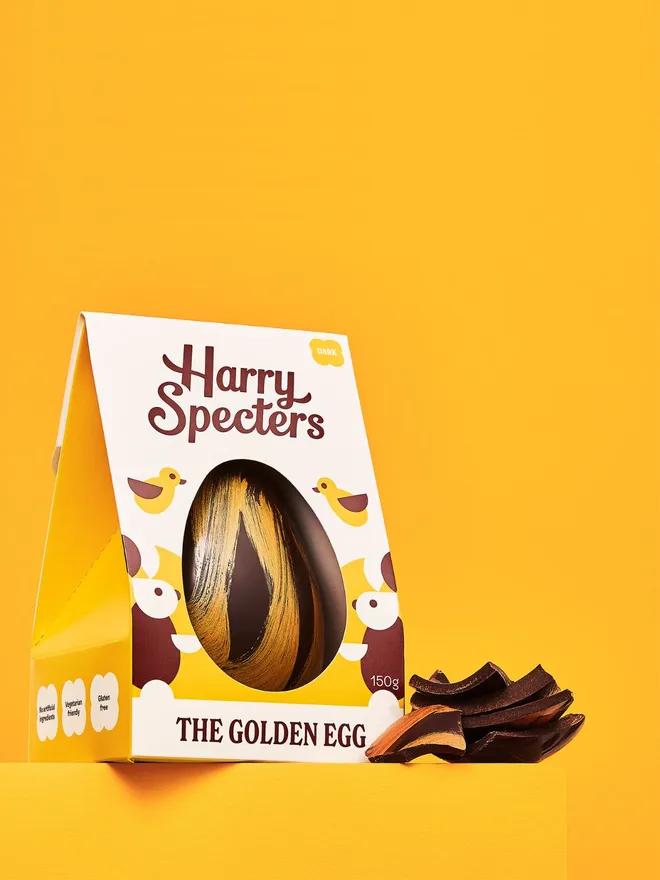 A dark chocolate Easter egg decorated with gold cocoa butter, next to a stack of dark chocolate Easter egg pieces
