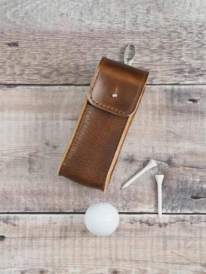 Handmade leather golf ball holder, shows 3 golf balls stacked on top of each other to the side of the case to represent the height of the leather pouch.