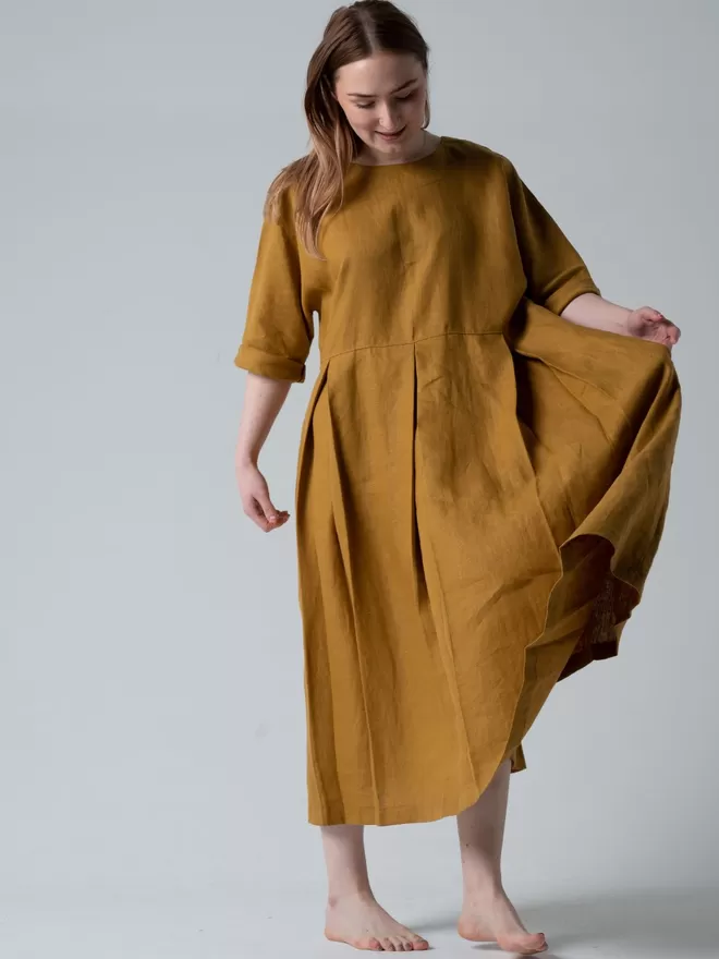 Midi length luxury linen dress in golden colour.  Deep pleated skirt and elbow length sleeves. Studio front view