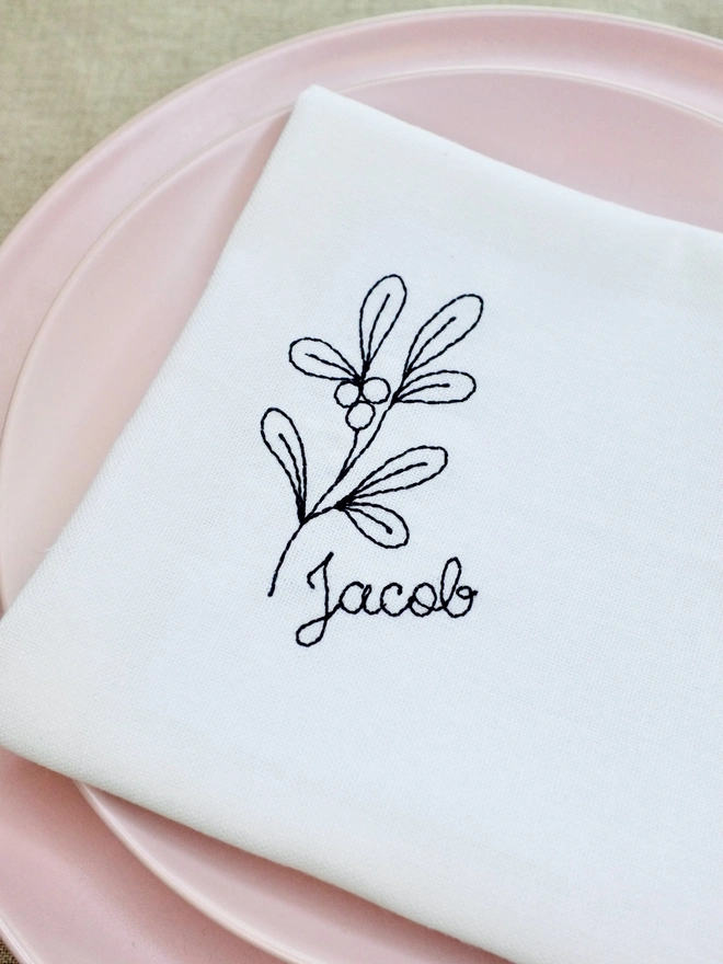 Mistletoe embroidered napkin with custom name in black cursive text, cotton Christmas napkin