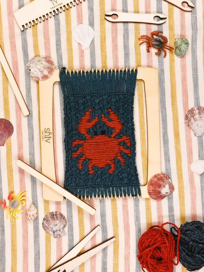seaside weaving kit. a green weave piece with a red crab photographed on a loom.