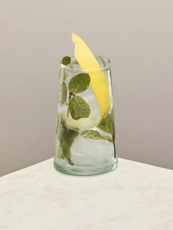 Highball Glasses (Set Of 1 Or 4), a highball glass sitting on a plain counter top against a white backdrop. It is filled with a soft drink. 