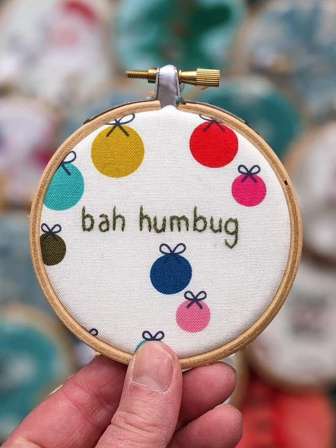 A hand embroidered hoop on Christmas fabric reading bah humbug