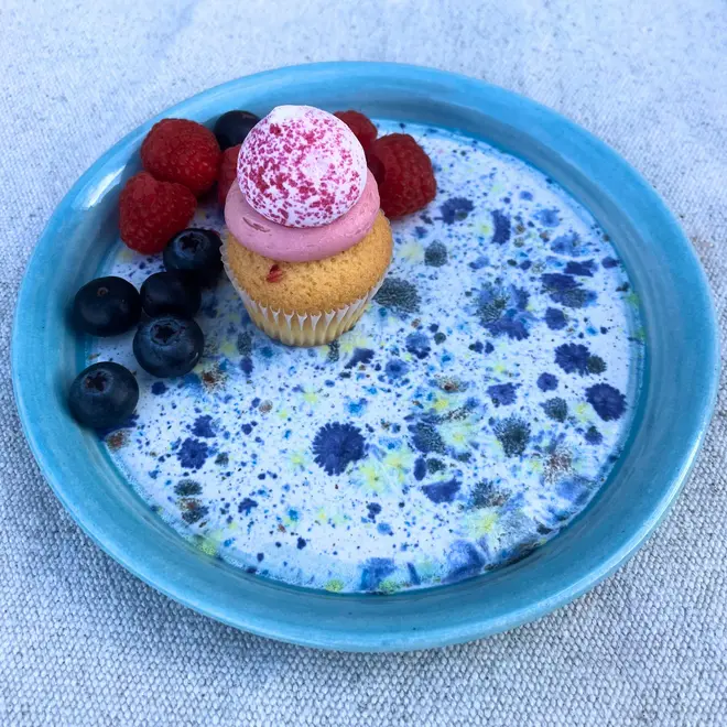 Shoreline Side Plate, a colourful plate placed on a stone surface. It is accompanied by fruits and a sweet treat. 