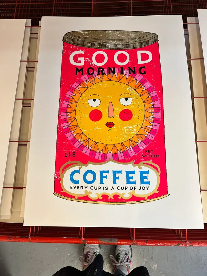 Sun Coffee Tin Good Morning Sunshine, a colourful coffee tin design on a white screenprint. It sits on a studio rack. 