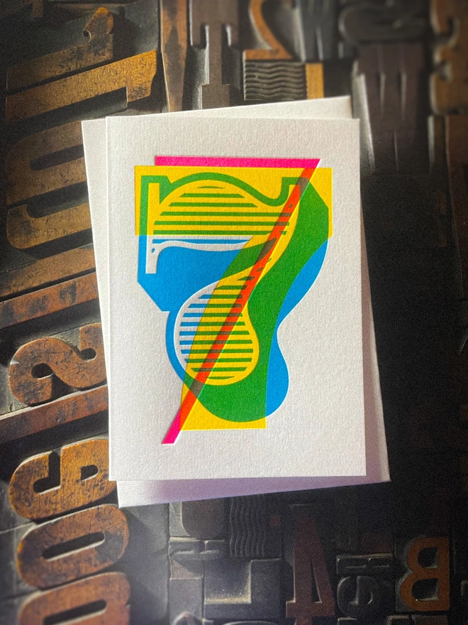 Handmade letterpress 7th birthday card featuring bold overlapping numerals printed in vibrant fluorescent cyan, magenta and yellow inks. Each card is individually hand printed using traditional letterpress techniques on luxury paper stock, creating a beautifully tactile finish with a deep impression and rich layered colours inspired by the CMYK printing process. Printed on a traditional letterpress from 1915. A wonderful artisan printed birthday card.