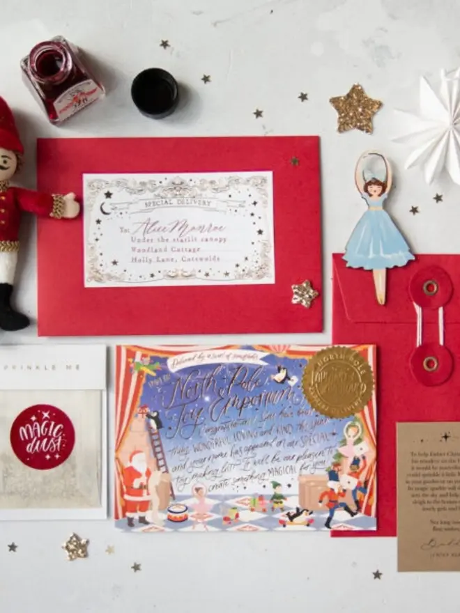 An overhead view of a letter from Father Christmas kit: a red envelope with a personalised gold foil "Special Delivery" label, the illustrated notecard with a gold seal, a red string-and-washer envelope, a Magic Dust bag and an instruction card, with a felt nutcracker and a ballerina decoration.