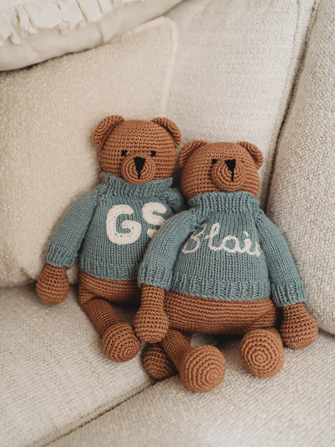 two hand crochet brown teddy bears on beige sofa with hand knit personalised jumpers